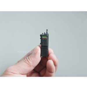 May include: A black walkie talkie with a green and red display screen. The walkie talkie has a small antenna on top.