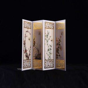 Peut inclure: Un paravent pliant blanc à quatre panneaux. Chaque panneau présente un motif d'inspiration chinoise différent avec des accents dorés. Les motifs comprennent une branche fleurie, un oiseau, du bambou et des chrysanthèmes. Les panneaux sont décorés de volutes dorées et des caractères chinois pour "printemps", "été", "automne" et "hiver".