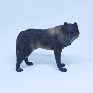 Op de afbeelding: Zwarte en bruine wolf figuur. De wolf staat op een witte achtergrond. De figuur is gemaakt van plastic en heeft een realistisch uiterlijk.