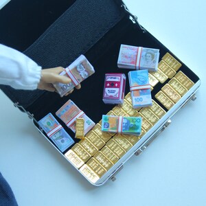 May include: Miniature open black briefcase filled with stacks of play money, gold bars, and a deck of playing cards. The play money includes various currencies, and the gold bars are arranged neatly inside the case.