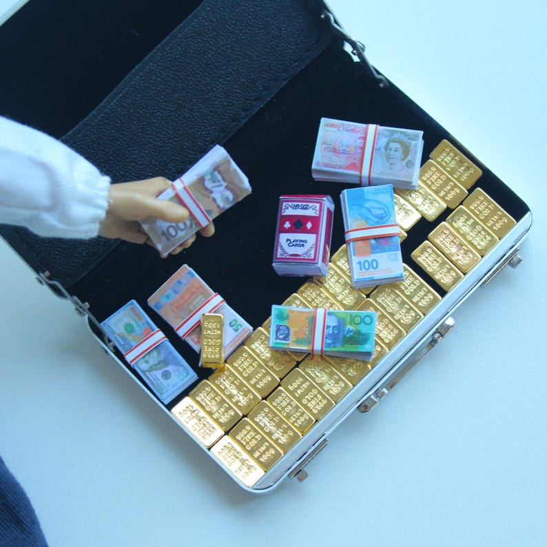 May include: Miniature open black briefcase filled with stacks of play money, gold bars, and a deck of playing cards. The play money includes various currencies, and the gold bars are arranged neatly inside the case.