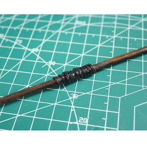 May include: A wooden stick wrapped with black leather or rubber bands. The stick is lying on a green cutting mat.