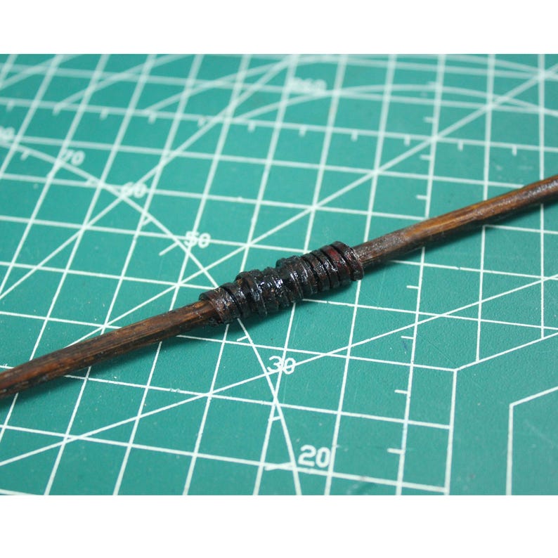 May include: A wooden stick wrapped with black leather or rubber bands. The stick is lying on a green cutting mat.