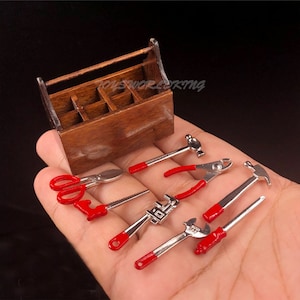 May include: A miniature wooden toolbox with a handle, containing a set of miniature tools with red handles, including a hammer, pliers, wrench, saw, and scissors.