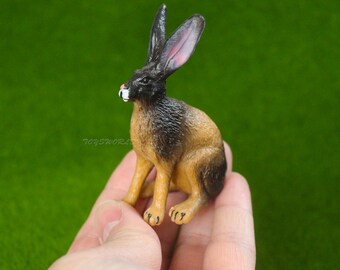 May include: A brown and black plastic toy rabbit figurine with long ears. The rabbit is sitting on its hind legs with its front paws tucked in.