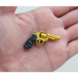 以下が含まれることがあります： 黒いプラスチック製のグリップが付いた金色のリボルバー。銃は小さく、手のひらに収まります。
