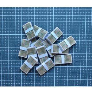 May include: A collection of miniature stacks of paper currency, each secured with a white band. The bills feature a portrait and text, arranged on a blue grid surface.