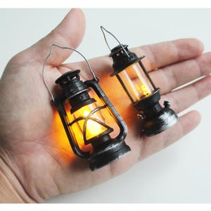 Peut inclure: Deux lanternes miniatures de style antique avec une lumière chaude et brillante. Les lanternes sont noires avec des accents argentés et des panneaux de verre transparents. Chaque lanterne a une poignée en métal pour le transport.