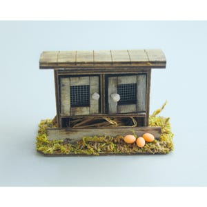 K&ouml;nnte beinhalten: Ein Miniatur-H&uuml;hnerstall aus Holz mit zwei T&uuml;ren, Drahtgitterfenstern und einem schr&auml;gen Dach. Der Stall steht auf einer Basis, die mit gr&uuml;nem Moos und Stroh bedeckt ist, mit drei orangefarbenen Eiern davor.