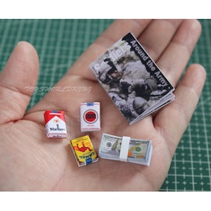 Op de afbeelding: Een miniatuurset met items, waaronder een pakje Marlboro-sigaretten, een pakje Camel-sigaretten, een bundel Amerikaanse dollarbiljetten en een tijdschrift met de titel "Around the Army".