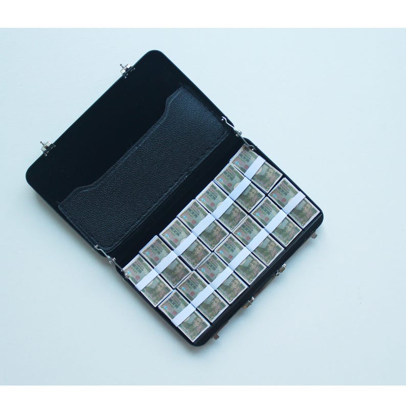 May include: Black leatherette case, open to reveal a grid of small, rectangular watercolor paint pans. The pans are arranged in rows and columns, each wrapped with a white paper band. The case has a black interior and a small pocket.