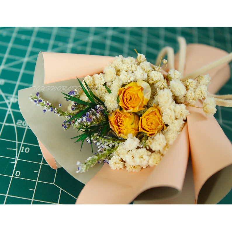 K&ouml;nnte beinhalten: Ein kleiner Strau&szlig; getrockneter Blumen, verpackt in pfirsichfarbenem Papier. Der Strau&szlig; enth&auml;lt gelbe Rosen und wei&szlig;en Schleierkraut.
