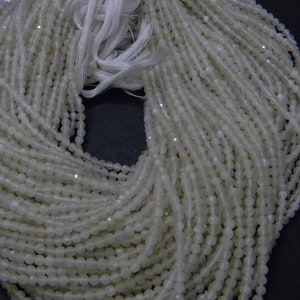 May include: A large bundle of off-white, faceted beads strung together, with a white string at the top. The beads have a subtle shimmer, and the strands are densely packed. The background is dark.