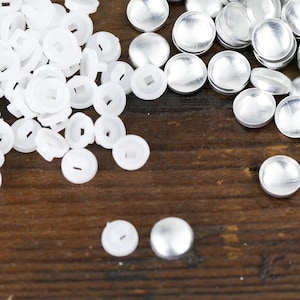 Peut inclure: Un tas de boutons-pression en plastique blanc et un tas de boutons-pression en métal argenté.