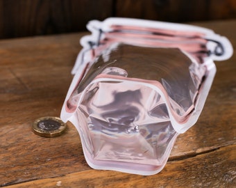 May include: A clear plastic reusable food storage bag with a pink and white design that looks like a glass jar. The bag is lying on a wooden surface.
