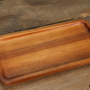 Könnte beinhalten: Ein rechteckiges Holztablett mit einer natürlichen Holzoptik. Das Tablett hat eine glatte Oberfläche und leicht abgerundete Kanten.