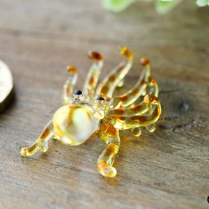 Pu&ograve; includere: Una piccola statuina di polpo in vetro di colore giallo e marrone. Il polpo ha otto tentacoli e occhi neri.