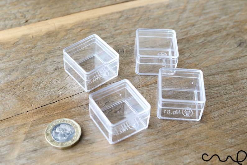 May include: Four clear plastic square boxes with lids. The boxes are approximately 1.5 inches in size. A British one pound coin is in the lower left corner of the image for scale.