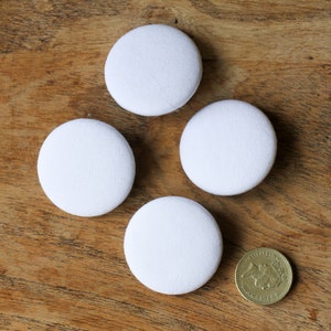Peut inclure: Quatre boutons ronds en tissu blanc sur une surface en bois.