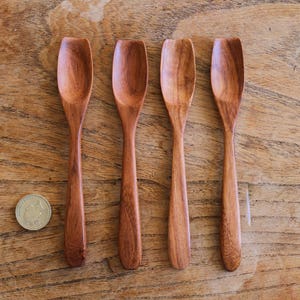 Puede incluir: Cuatro cucharas de madera con un cuenco redondeado y un mango largo y estrecho. Las cucharas est&aacute;n dispuestas en fila sobre una superficie de madera.