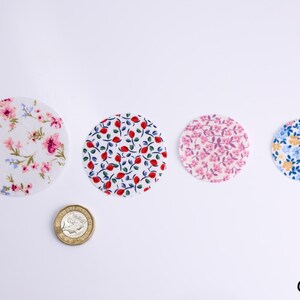 Peut inclure: Quatre cercles en tissu avec différents motifs floraux. Les cercles sont disposés en rangée de gauche à droite. Les cercles sont blancs avec des fleurs roses, rouges, bleues et jaunes.