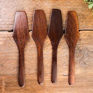 May include: Four dark brown wooden spreaders with flat, tapered blades and smooth, rounded handles. Each utensil displays a distinct natural wood grain pattern, showcasing varying shades of deep mahogany and walnut tones in a uniform design.