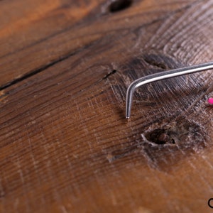 Op de afbeelding: Een close-up van een roze en zilveren haaknaald op een houten oppervlak.