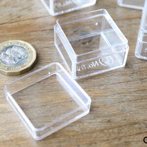May include: Four clear plastic square boxes with lids. The boxes are small and have the text "13.01" printed on the bottom.