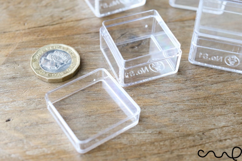 May include: Four clear plastic square boxes with lids. The boxes are small and have the text "13.01" printed on the bottom.