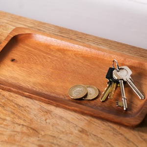 May include: A wooden tray with a natural finish, featuring a set of keys and two coins. The tray is rectangular and has rounded edges.