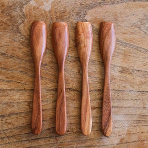 Puede incluir: Cuatro cucharas de madera con bordes redondeados y un acabado de madera natural. Las cucharas est&aacute;n dispuestas en una fila sobre una superficie de madera.
