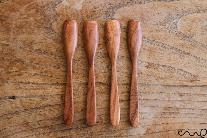 Puede incluir: Cuatro cucharas de madera con bordes redondeados y un acabado de madera natural. Las cucharas est&aacute;n dispuestas en una fila sobre una superficie de madera.