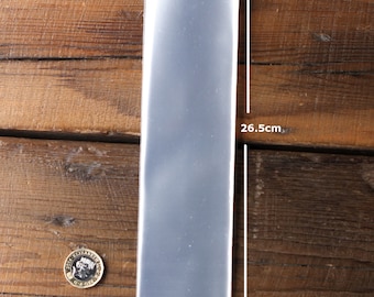 Puede incluir: Una funda de plástico transparente que mide 26,5 cm por 5,3 cm. La funda está colocada sobre una superficie de madera.