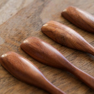 Puede incluir: Cuatro cucharas de madera de color marr&oacute;n rojizo. Las cucharas est&aacute;n dispuestas en fila sobre una superficie de madera.