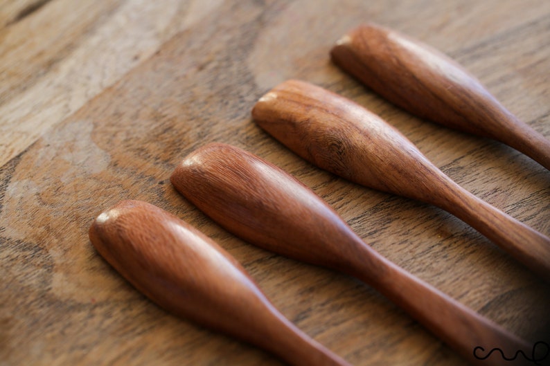 Puede incluir: Cuatro cucharas de madera de color marr&oacute;n rojizo. Las cucharas est&aacute;n dispuestas en fila sobre una superficie de madera.