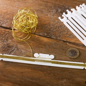 Op de afbeelding: Een verzameling knutselspullen op een houten oppervlak. De afbeelding toont een spoel gouden metallic draad, witte plastic draad organizers en een munt. De draad is op een witte plastic organizer gewikkeld.
