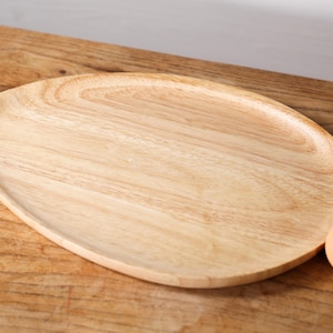 Może przedstawiać: Okrągła drewniana taca do serwowania w jasnobrązowym kolorze. Taca wykonana jest z naturalnego drewna i ma gładkie, polerowane wykończenie.