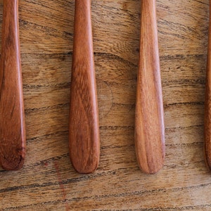 Puede incluir: Cuatro cucharas de madera con un acabado marr&oacute;n rojizo, dispuestas sobre una superficie de madera.