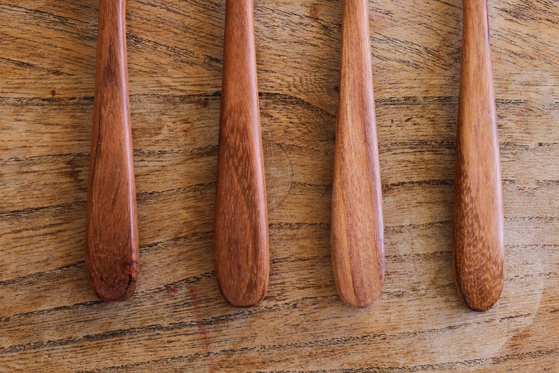 Puede incluir: Cuatro cucharas de madera con un acabado marr&oacute;n rojizo, dispuestas sobre una superficie de madera.