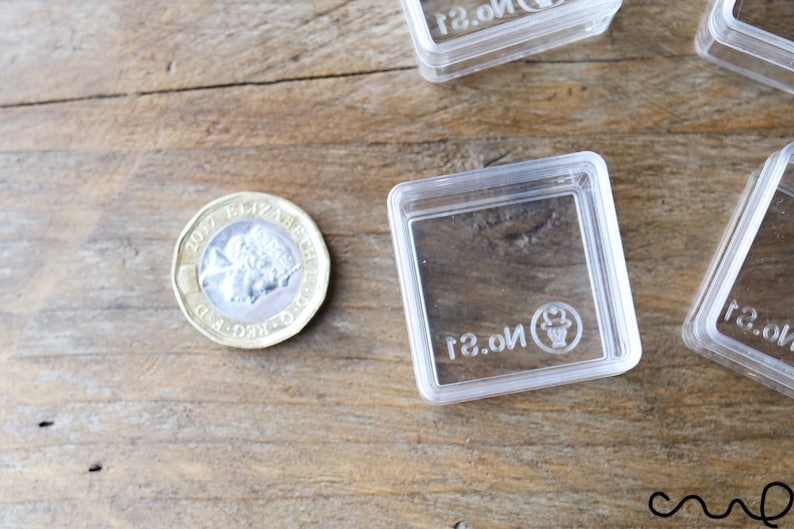 May include: A close-up of a British one pound coin with the inscription "2017 ELIZABETH II D.G. REG. F.D."  The coin is lying on a wooden surface next to a clear plastic square box with the text "No. 21" printed on the bottom.