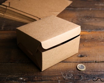 May include: A brown cardboard box with a hinged lid. The box is sitting on a wooden surface.