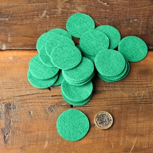 May include: A pile of green felt circles on a wooden surface. A British coin is in the foreground.