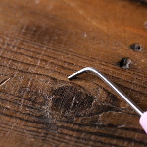 Puede incluir: Primer plano de un gancho de ganchillo rosa con un gancho de metal plateado. El gancho est&aacute; sobre una superficie de madera.