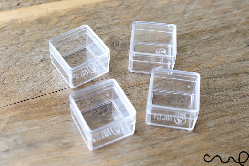May include: Four clear plastic square boxes with lids. The boxes are empty and are sitting on a wooden surface.