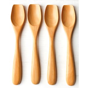 Può includere: Quattro cucchiai di legno marrone chiaro disposti verticalmente su uno sfondo bianco. Ogni cucchiaio ha un manico arrotondato e una cavità rettangolare. Questi cucchiai di legno sono probabilmente destinati alla cucina.