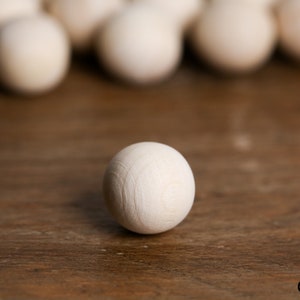 Könnte beinhalten: Eine einzelne weiße Holzkugel auf einer braunen Holzoberfläche. Die Kugel ist glatt und rund, mit einer leichten Maserung.