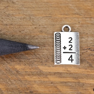 May include: Silver charm shaped like a notebook with the equation 2 + 2 / 4 on the front.