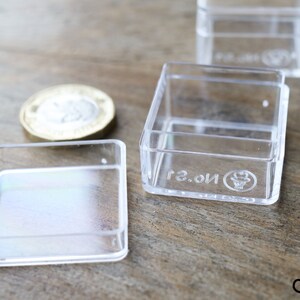 May include: Four clear plastic square boxes with a raised lip around the edge. The boxes are empty and have a small logo on the bottom that says "No. 2".