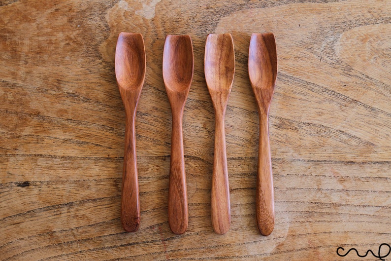 Puede incluir: Cuatro cucharas de madera con bordes redondeados y un color marr&oacute;n natural. Las cucharas est&aacute;n dispuestas en una fila sobre una superficie de madera.