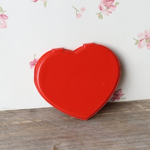 Puede incluir: Un espejo compacto de corazón rojo.